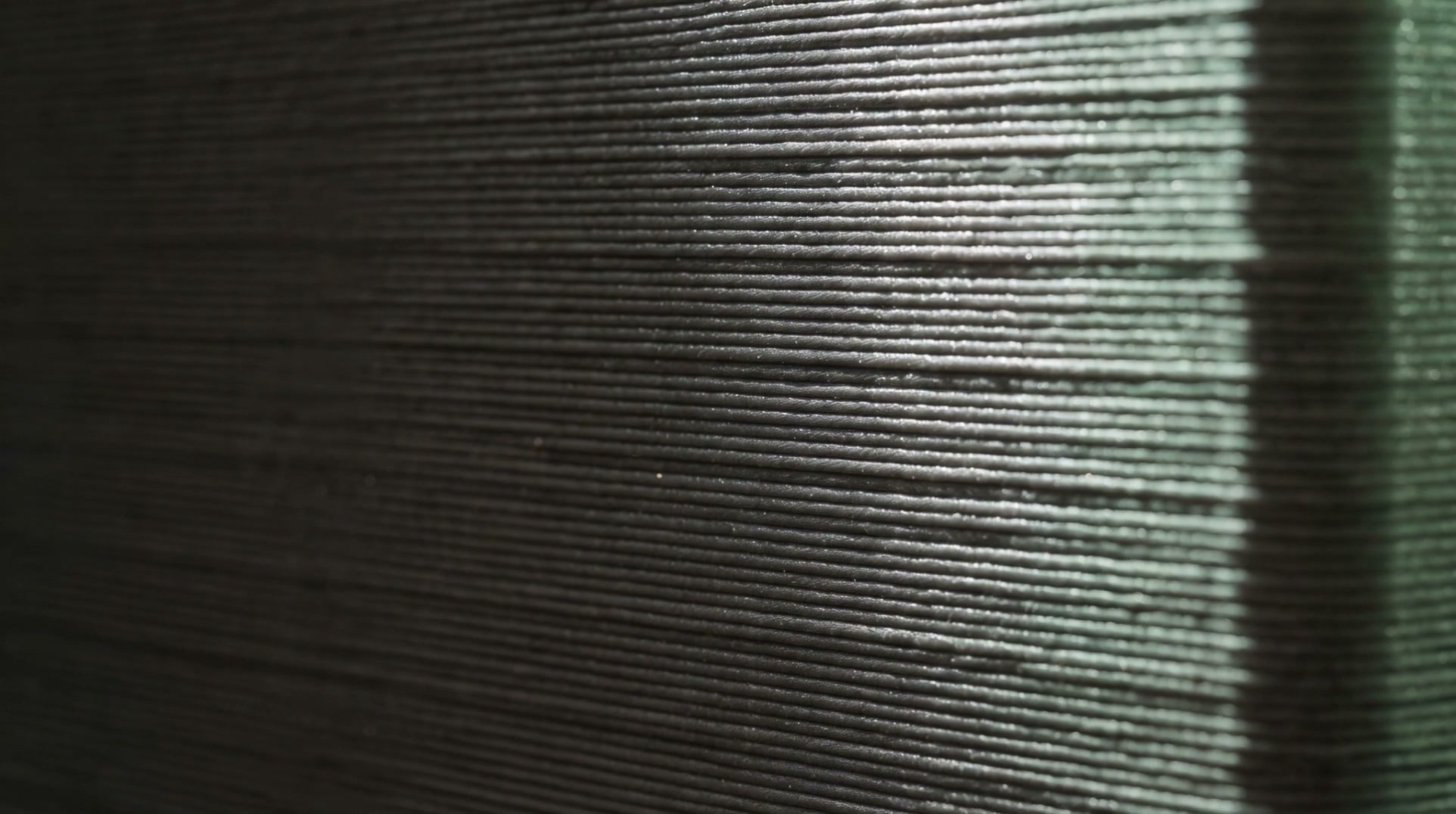 A close view of a printed charcoal surface, showing hundreds of fine stacked layer lines catching the light.
